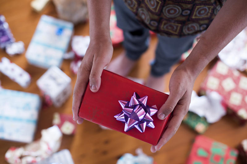 A close up, point of view shot of a teenager handing a Christmas gift.