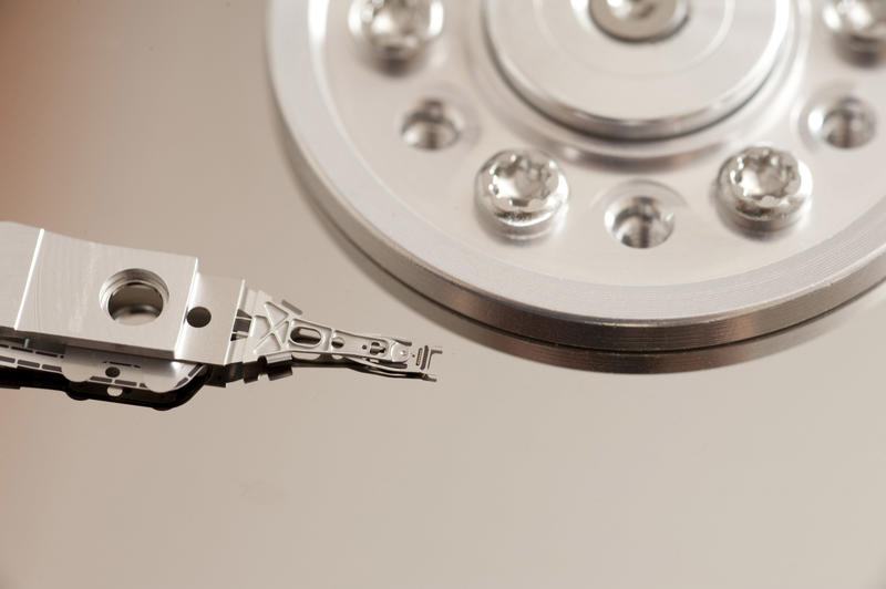 Close-up view of shiny metal hard disk drive reading head near disk mount with screws