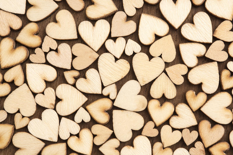 Pattern of little wooden hearts cut of unpainted plywood spread all over dark table surface, love background concept