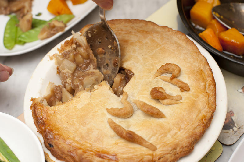 Delicious homemade meat pie with flaky crust being spooned into nearby plates with snap peas and butternut squash