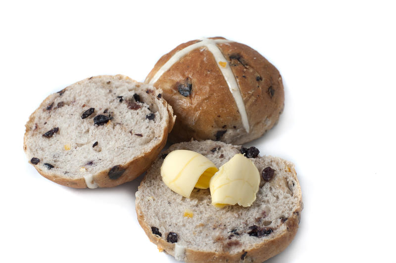 Sliced and buttered spicy fruity Hot Cross bun for Easter with a whole one behind showing the symbolic pastry cross over a white background