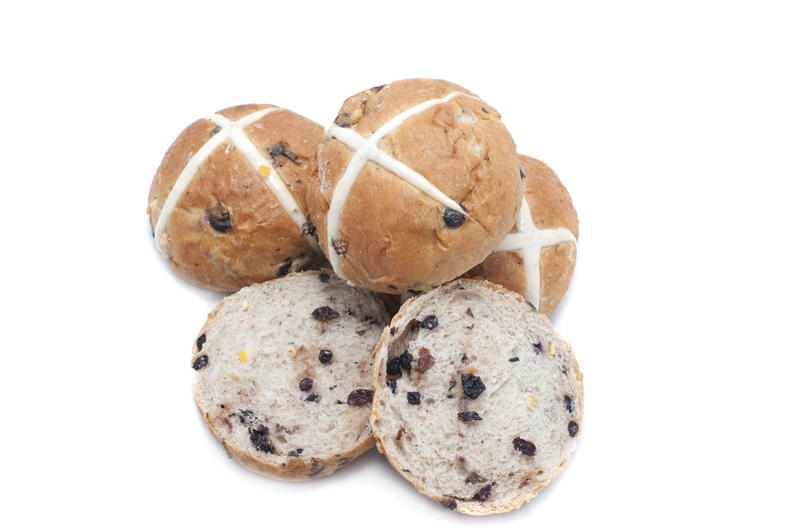 Fresh baked delicious fruity Easter Hot Cross Buns with one slice open to show the raisins and the others arranged to show the cross symbolic of the Crucifixion, on white with copy space
