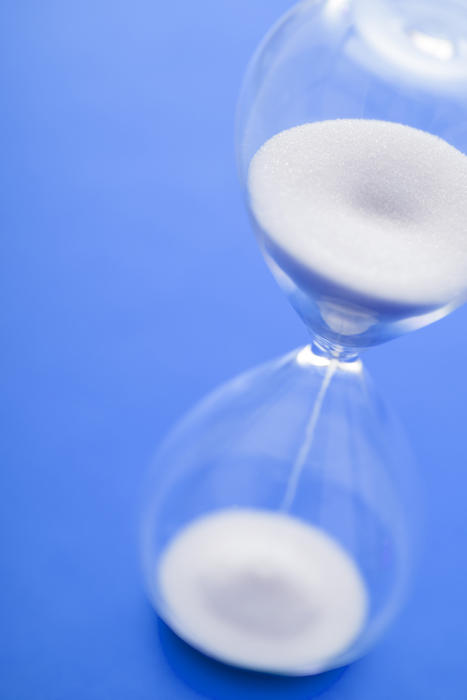White grains of sand running through an hourglass or egg timer over a blue background in an angled view from above
