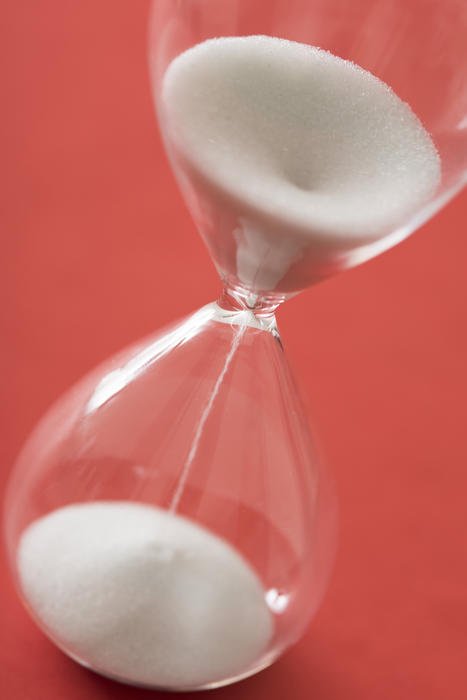 White grains of sand running through an hourglass or egg timer measuring passing time counting down to a deadline, over a red background