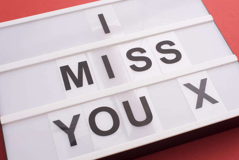 Close-up view of small white lightbox with I Miss You X message sign of black changeable letters over red background, missing about ex concept