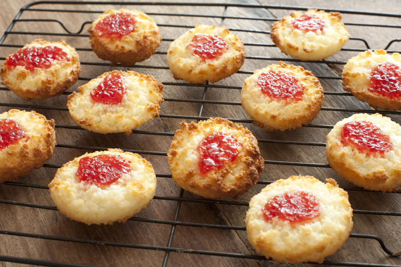 Freshly baked delicious coconut strawberry jam cookies spread out on oven tray over brown table