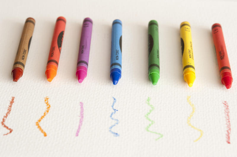 Still Life of Colorful Crayons Lined Up in front of Corresponding Scribbles on White Paper with Copy Space