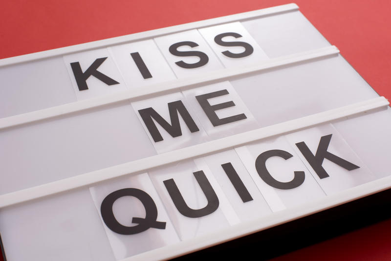 White lightbox table with changeable KISS ME QUICK sign of black letters, close-up on red surface