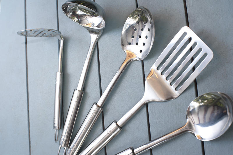 Set of stainless steel kitchen utensils or cookware arranged in a fan viewed at an oblique low angle on slatted grey wood