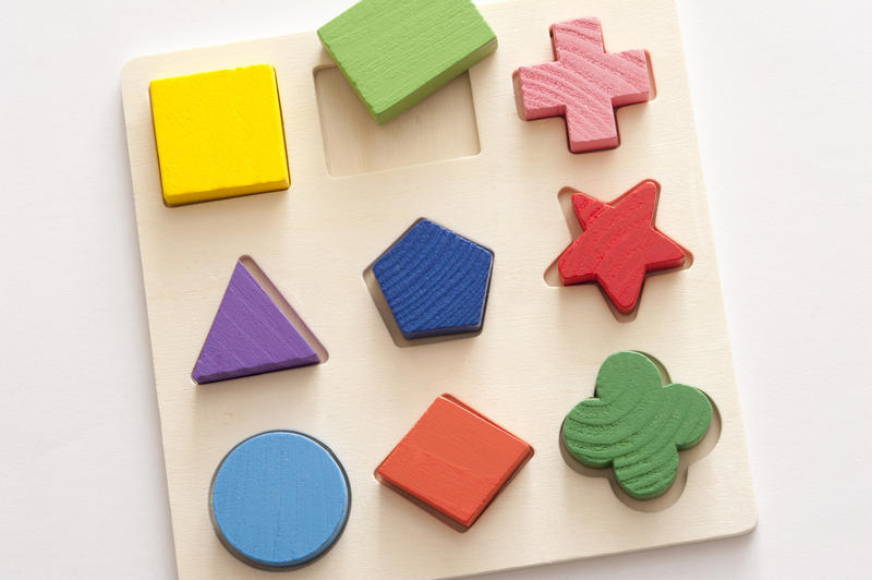 Learning puzzle with nine different colorful basic shapes and cutouts in wood viewed from overhead on white
