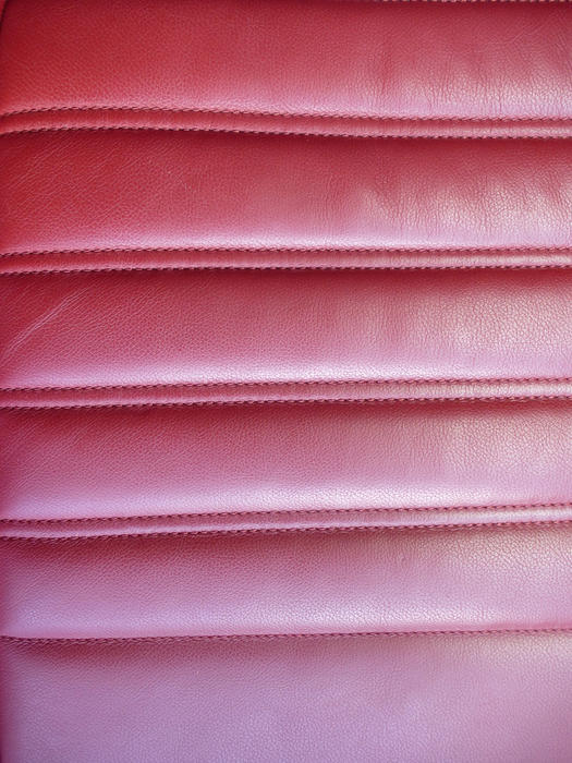 Red leather car upholstery in a ridge formation for the back of the front seats of the vehicle, close up full frame view