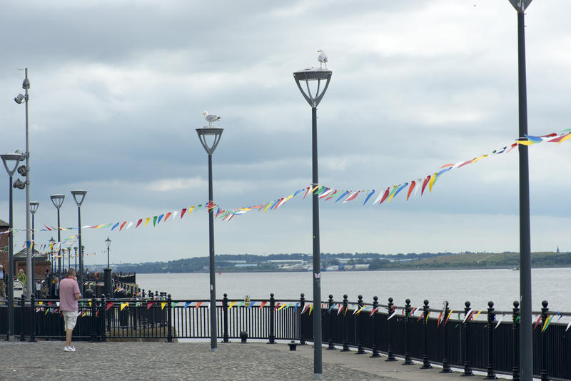 Liverpool, UK, Mersey waterfront on a cloudy day with festive bunting strung between the lampposts lining the promenade overlooking a calm ocean