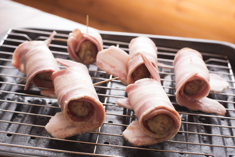 Preparing pigs in blankets on a wire rack with cured ham around pork sausages waiting to be grilled or oven baked