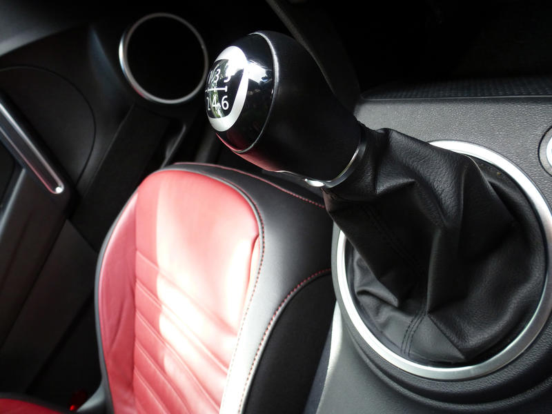 Manual car gear shift in a modern car with black upholstery with red leather trim on the seats