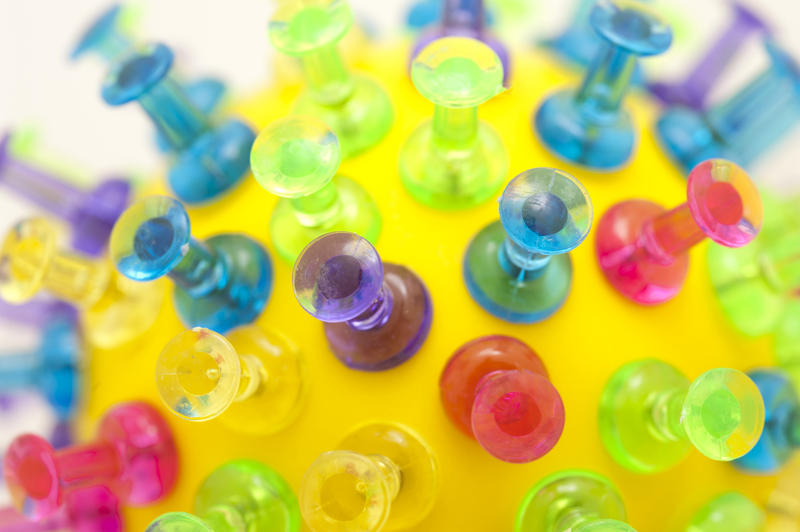 Purple, green, blue, pink and yellow plastic push pins stuck into round yellow ball