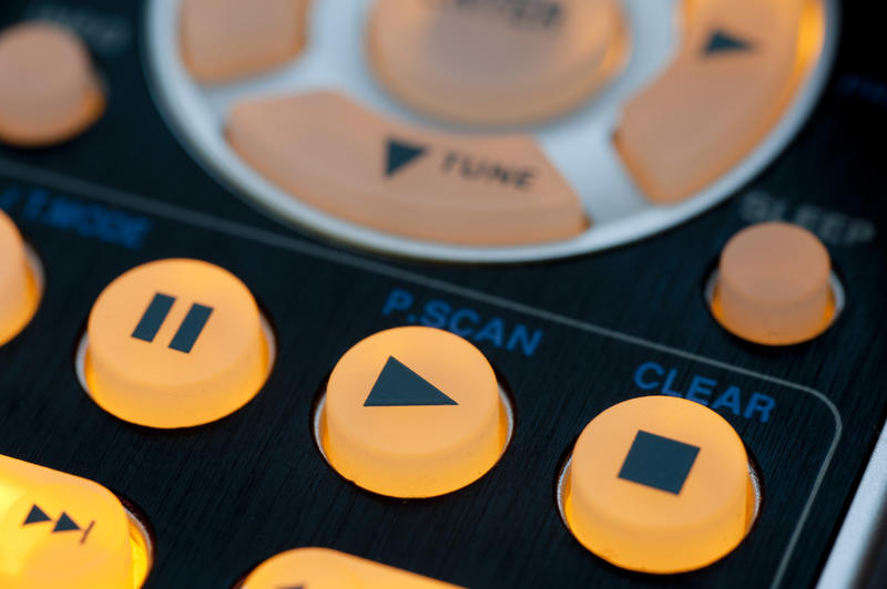 Yellow illuminated playback control buttons on black remote control. Close-up full frame image