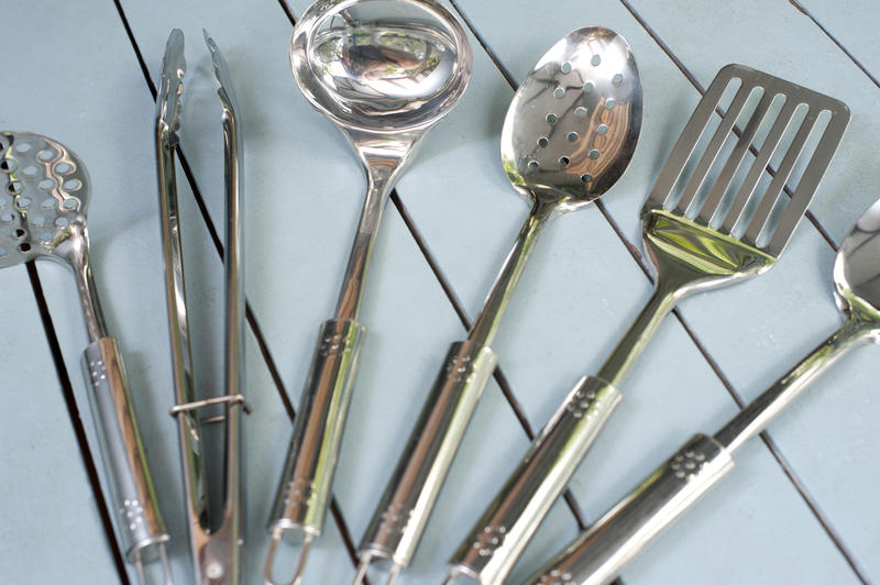 Set of metal cooking utensils fanned out on display on rustic grey slatted wood table