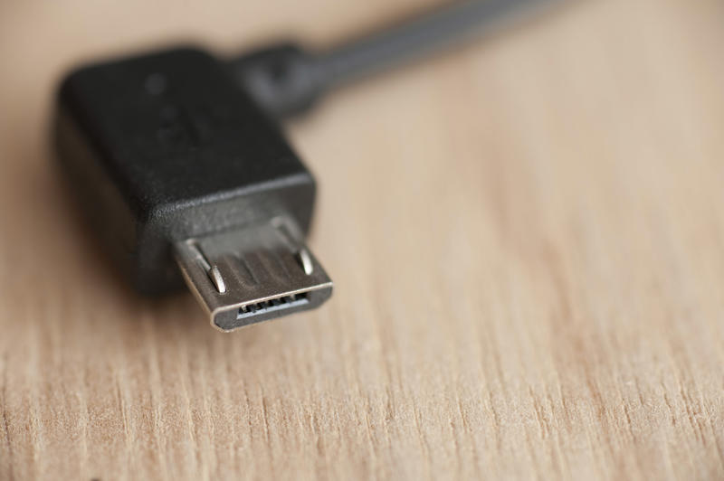 Micro USB connector with black wire, close-up macro shot on wooden table with copy space