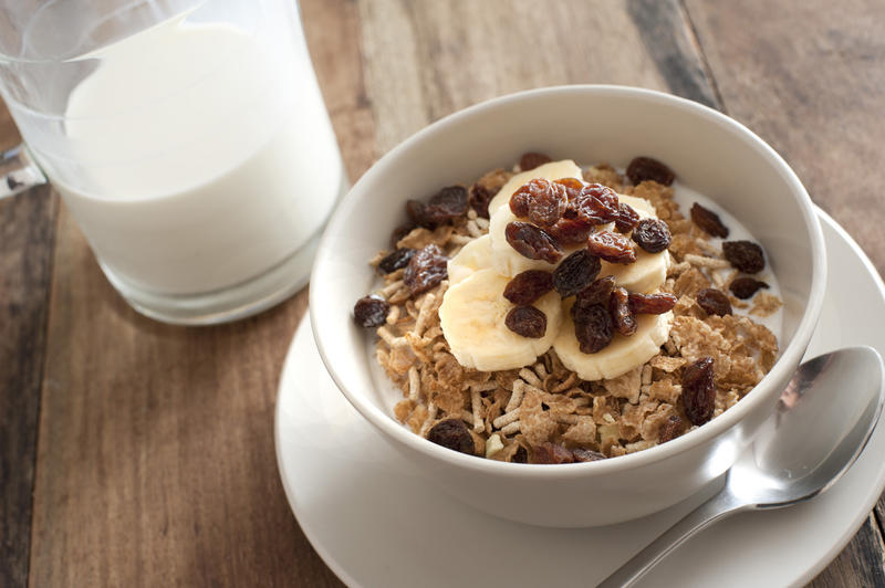 First person perspective view on breakfast of milk and cereal in bowl on table with saucer and spoon