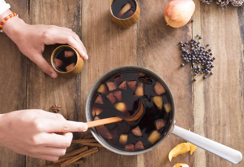 Person serving freshly made mulled red wine with spices and fruit in a pot using a ladle to spoon it into mugs to celebrate the holiday season