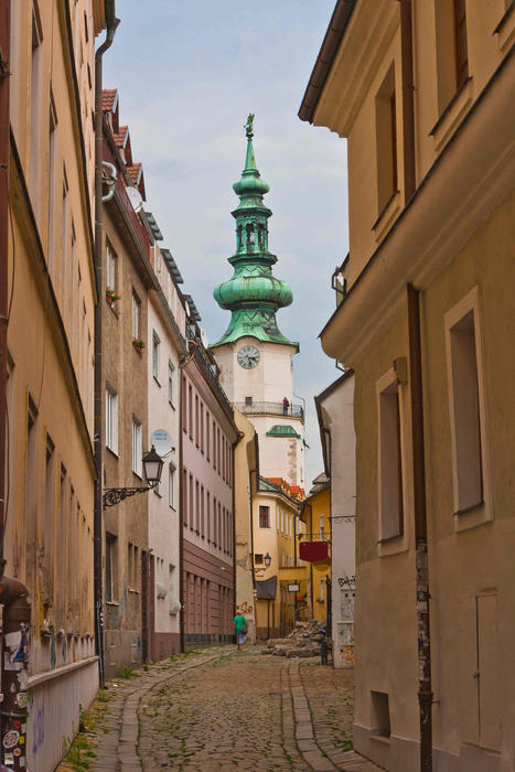 Narrow crooked cobbled bystreet with church tower in Bratislava