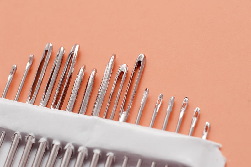 Macro Close Up of Eyes of Various Sewing Needles in Package on Orange Colored Background with Copy Space - Sewing and Embroidery Concept Image