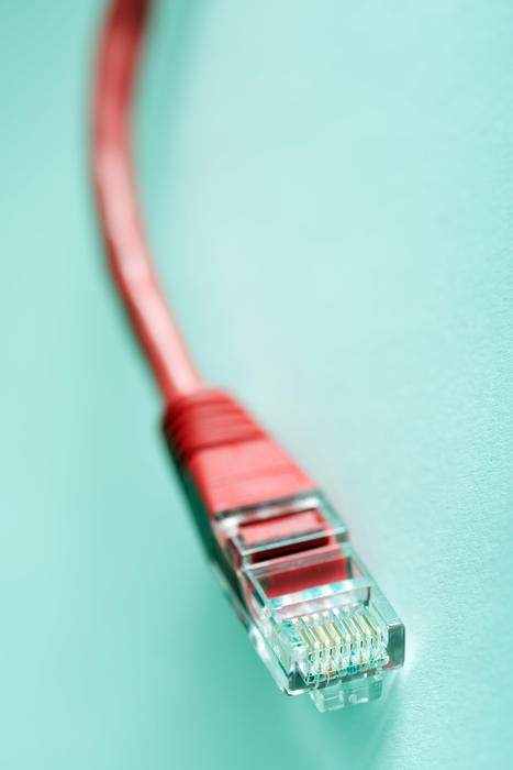 Red cable with LAN network connector over light blue or cyan background, close-up selective focus image