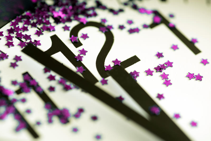 Clock decorated with purple stars striking midnight for a festive New Years Eve celebration with a close up view of the hands on the dial and the number 12