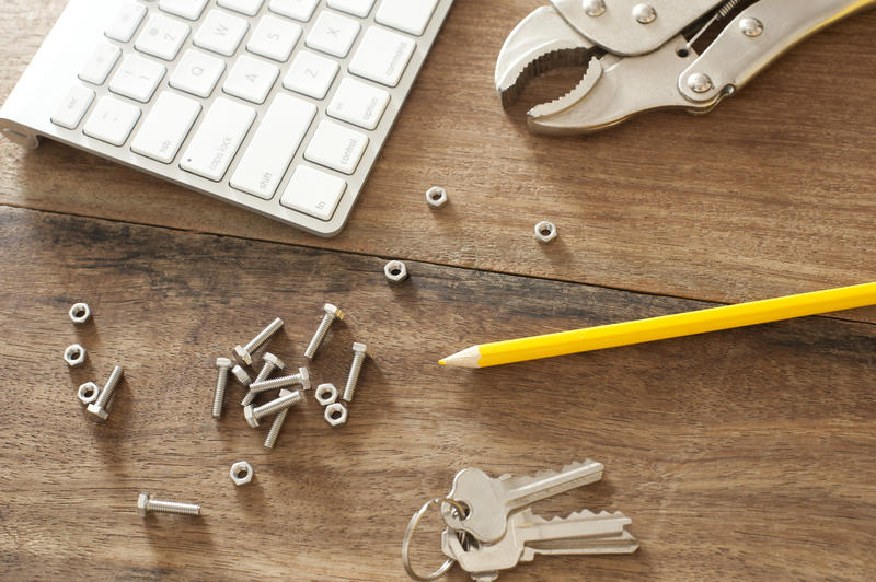 DIY tools background concept with scattered nuts, bolts, a mole grip, pencil, keys and computer keyboard on a wooden background, viewed from above