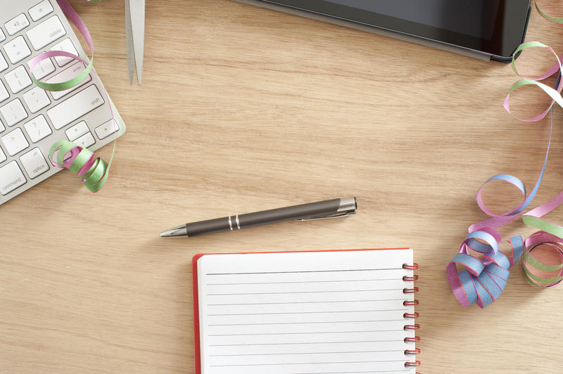 Conceptual office party background with a high angle view of a desk with keyboard, pen and notepad with colorful twirled party streamers