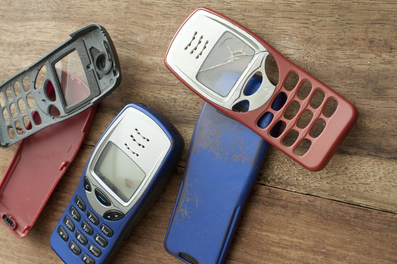 Casings and backs for old style mobile phones with buttons and dials on red , blue and black on a wooden table