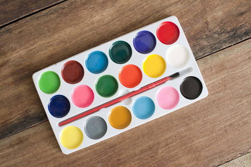 Single new plastic watercolor palette with paintbrush over wooden background at diagonal perspective