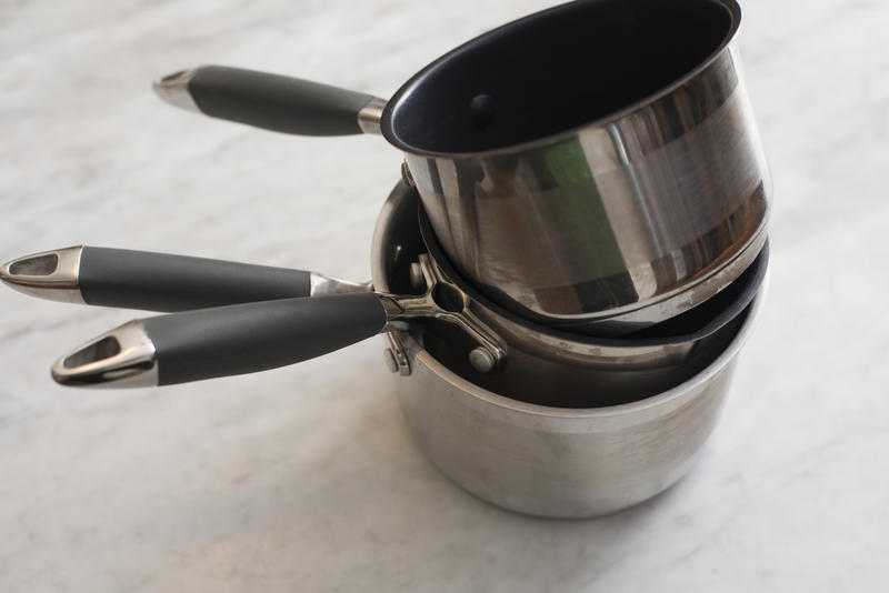 Stack of three metal non-stick kitchen pans or cookware with handles over a light grey background viewed high angle