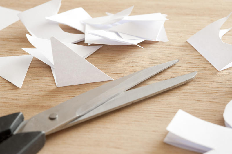 Close Up of Pair of Scissors on Wooden Table Surrounded by Scraps and Clippings of White Paper - Craft and Hobby Concept Still Life