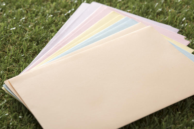 Fanned stack of colored Easter envelopes for seasonal wishes lying on green spring grass, blank copy space for your message