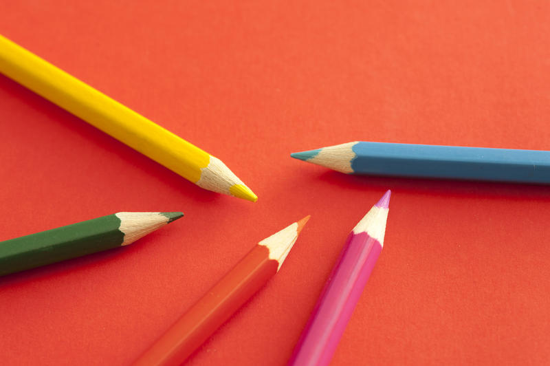 Randomly placed green, yellow, pink, blue and red colored pencils over bright orange background