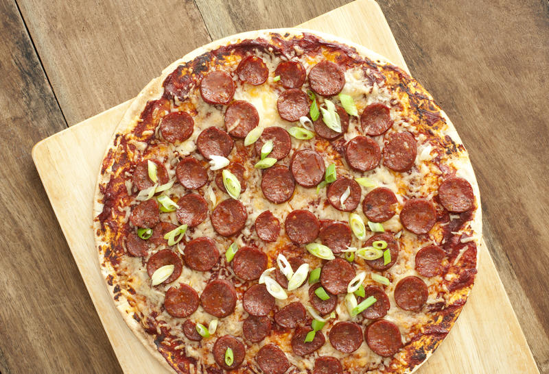 Delicious pastrami or salami Italian pizza topped with mozzarella cheese and shallots or diced onion viewed whole from above on a wooden cutting board