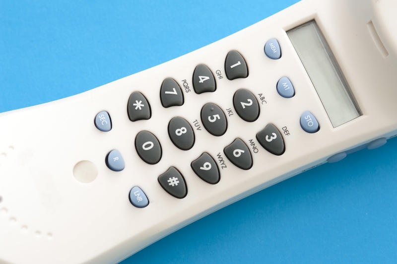 Phone dialpad on white handset with black rubber buttons, cropped close-up on blue background
