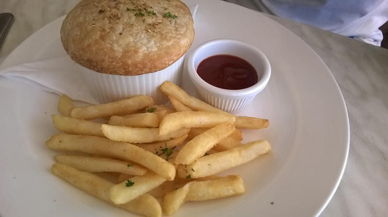 Fresh pile of golden crispy French fries served with a meat pie and side dish of tomato ketchup in a close up high angle view