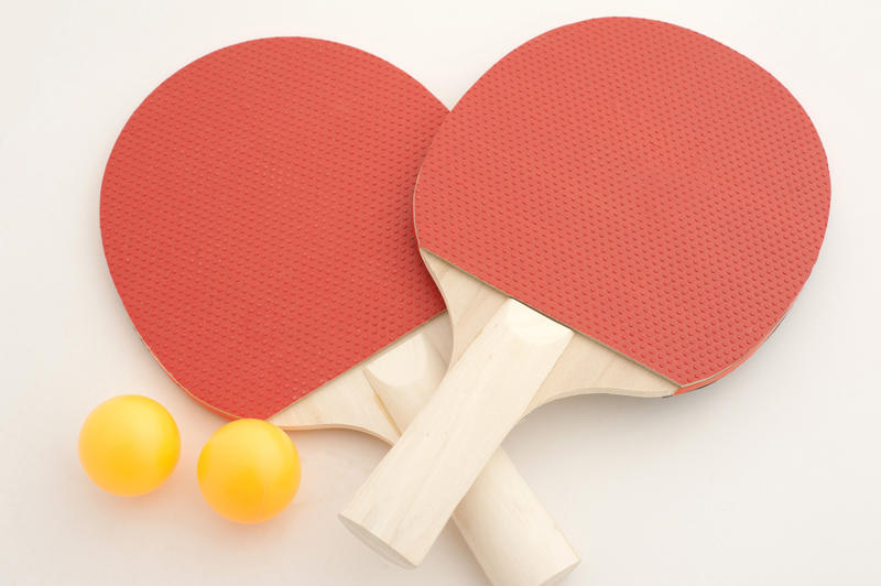 Two red table tennis bats with colorful yellow balls crossed over on a white background, close up view