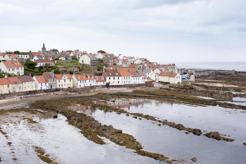 Scene of red roofed houses in Pittenweem Scotland during low tide. Muddy ridges remain where water once stood.