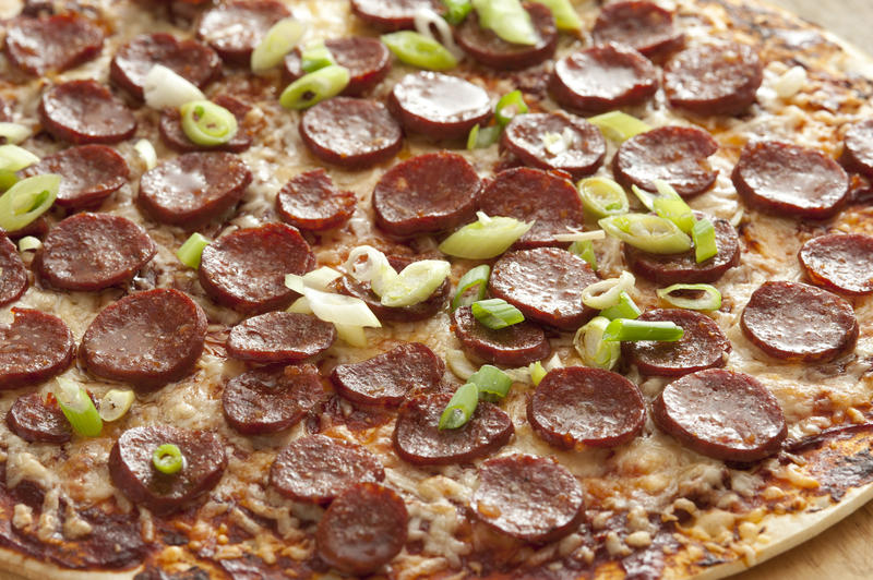 Full background of pepperoni cheese pizza garnished with green scallion onions and peppers