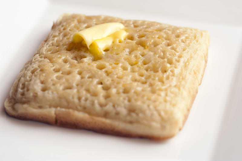 Macro close up view on fried square crumpet with soft butter melting into little holes on top inside plate