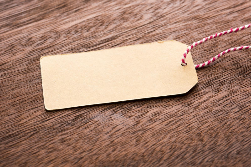 Blank brown gift tag or label with colorful red and white striped string and copy space for your message lying on textured wood