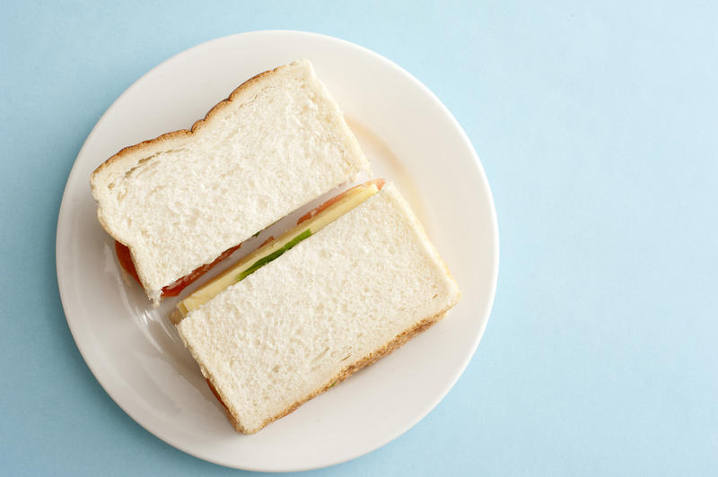 Appetizing white bread sandwich with cheese on a round white plate and against a light blue background as seen from an overhead view