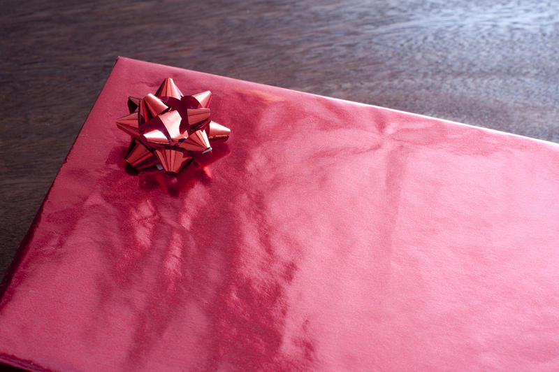 Present box wrapped with glossy red paper and decorated with red ribbon over lacquered table. Plain valentine gift concept with copy space