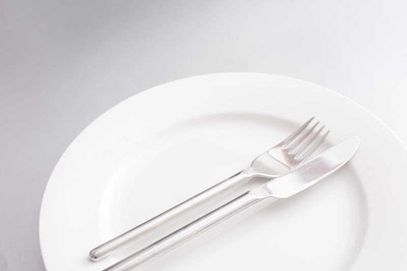 Clean generic white dinner plate with silver knife and fork neatly arranged in the centre in a close up cropped view