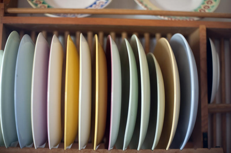 Wooden rack mounted on a wall with assorted colorful plates standing upright in a kitchen in a close up view