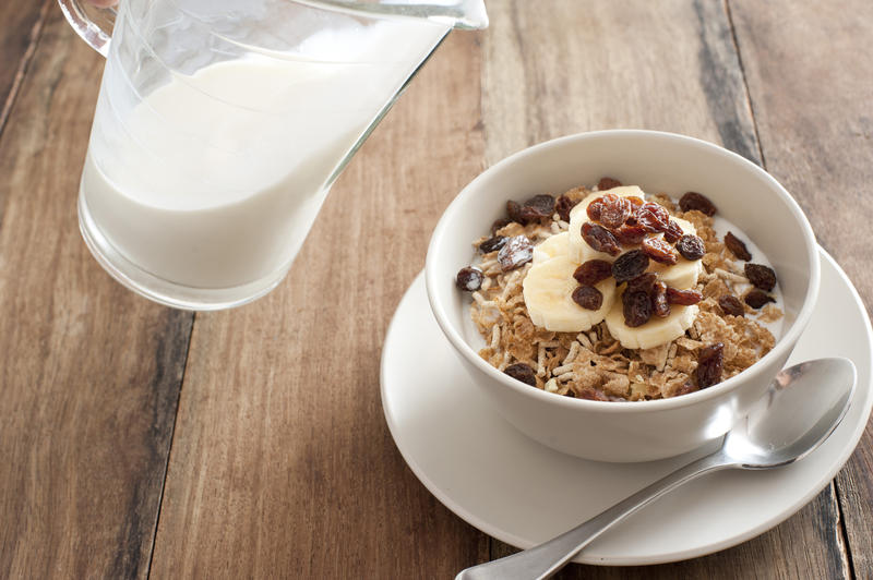 Healthy breakfast muesli topped with fresh bananas and dried raisins and served with milk from a jug alongside, high angle, view
