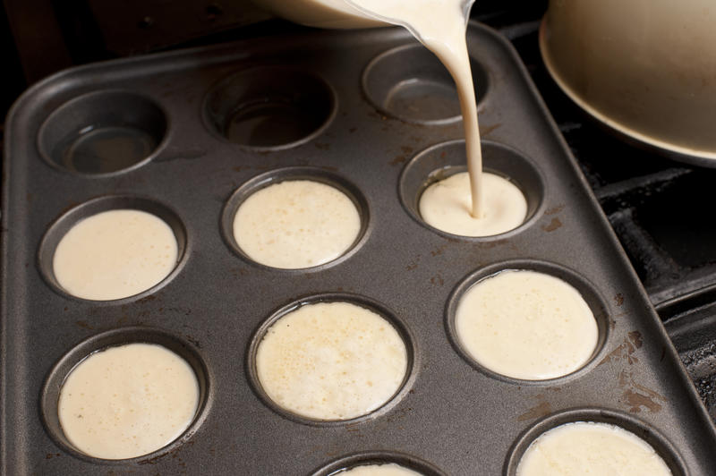 Cake batter being poured into muffin tin on stove top beside other cook ware
